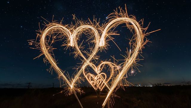Drawing sparkling heart trails with sparklers under starry sky for romantic celebration