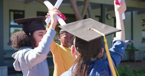 Multicultural teens celebrating graduation on campus with mortarboards and diplomas