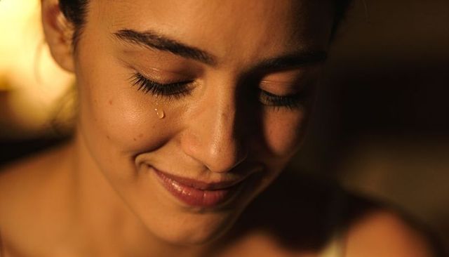 Smiling young woman shedding tear while closing eyes in warm intimate closeup