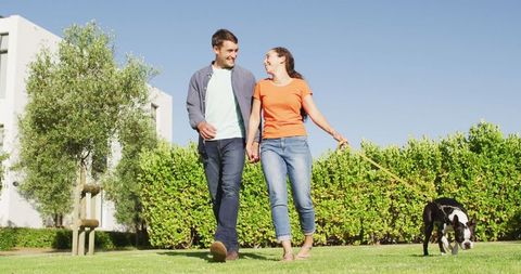 Happy couple strolling in sunlit park with stylish puppy
