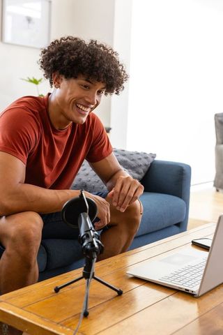 Young content creator recording podcast in modern living room with laptop and microphone