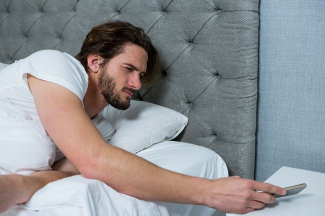 Man waking up with mobile alarm clock in bedroom at home