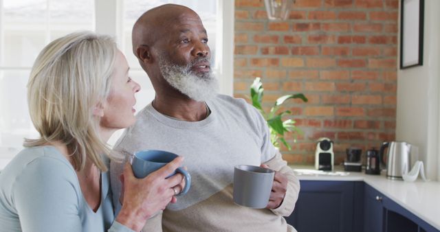 Older couple sitting together in kitchen, enjoying coffee and relaxing. The scene suggests a comfortable, happy home life. Perfect for use in lifestyle articles, advertisements for home products or coffee brands, and content promoting healthy, happy relationships among older adults.