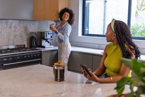 African american women making coffee in bright modern kitchen with espresso maker and marble island