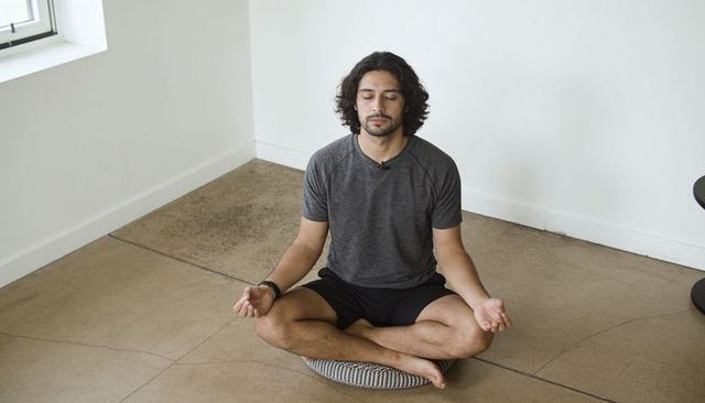 Meditating man practicing mindfulness on patterned cushion in sunlit minimalist studio