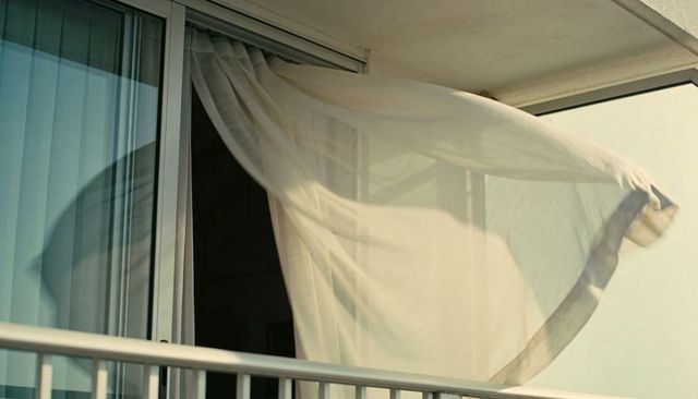 Sheer curtain billowing from balcony sliding door soft morning light translucent motion