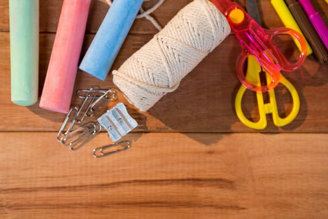 Assorted stationery supplies laid out on a wooden desk, including chalk, scissors, string, paper clips, and sharpener. Ideal for use in images related to school, crafting, education, office work, and organizational themes.