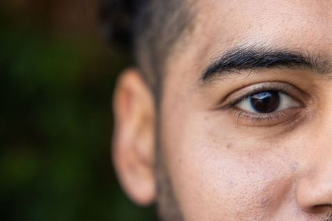Closeup male eye and facial stubble with green bokeh background, intimate headshot