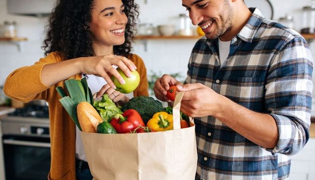 Young couple unpacking fresh groceries in bright kitchen, smiling while preparing meal