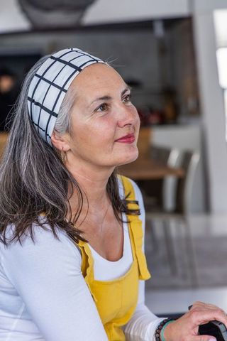 Reflective middle-aged woman wearing yellow overalls and checkered headband lifestyle portrait