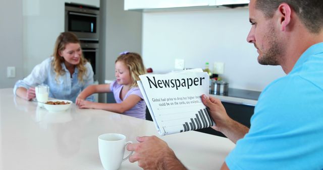 Father reading the newspaper while family has breakfast at home in the kitchen