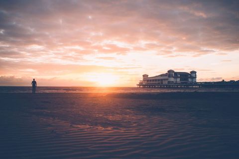Solitary Figure Walking Along Sunset Beach with Pier and Golden Sky