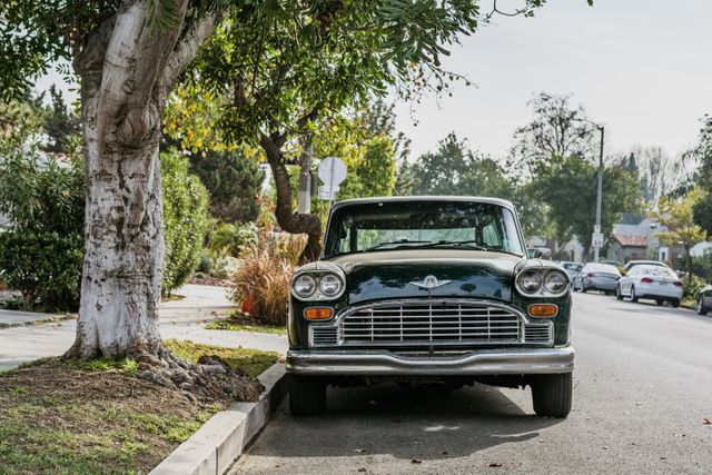 Vintage car parked on a tree-lined residential street on a sunny day. Urban neighborhood with subtle greenery and clear skies all add to a tranquil atmosphere. Suitable for concepts like classic automotive, retro transportation, suburban life, nostalgic scenes, and urban tranquility.