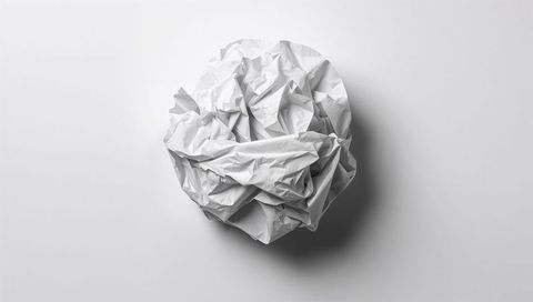 Crumpled white paper ball casting soft shadow on minimal light gray background