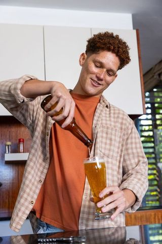 Young Red-Haired Man Pouring Beer in Modern Kitchen