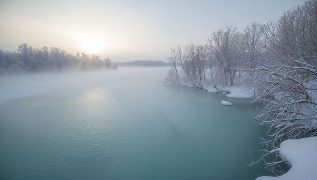 Teal River Flowing Through Snow-Covered Banks at Misty Sunrise Winter Landscape Panorama