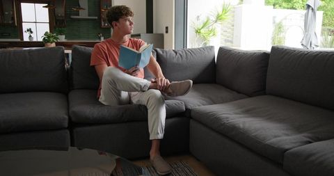 Young man reading on gray sectional sofa near sliding door in contemporary home interior