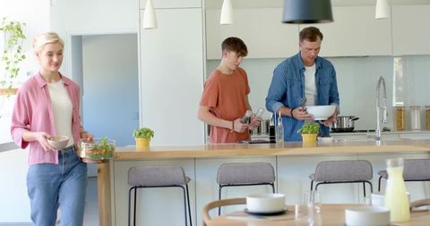 Family preparing meal together at bright modern kitchen island with herbs and seasoning