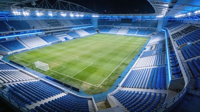 Floodlit modern football stadium shining at night with empty blue seats and pristine pitch