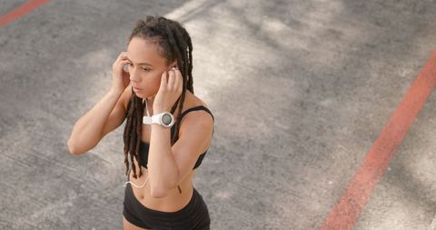 Young Woman with Earphones Standing Outdoors Wearing Sportswear