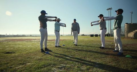 Baseball team stretching while coach leads warmup drills on field at golden hour