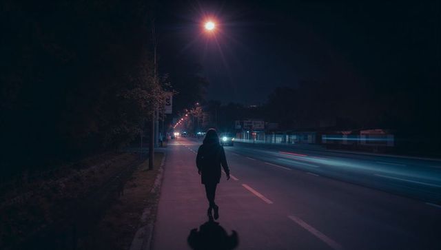 Hooded figure walking alone on urban night street with light trails