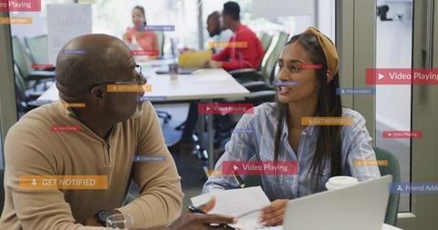 Colleagues discussing documents and reviewing laptop in glass-walled collaborative office
