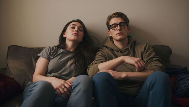 Young couple lounging on couch in neutral living room, casual outfits, moody cozy vibe