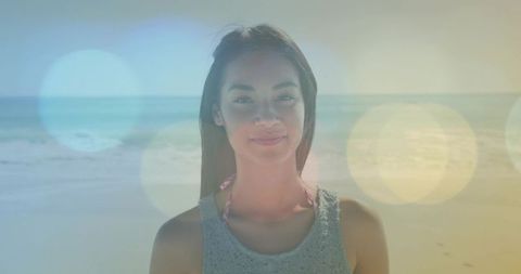 Vertical video: smiling woman posing on beach, pastel bokeh and backlit lens flare