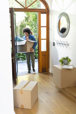 African american man carrying moving box entering arched door into sunlit modern foyer