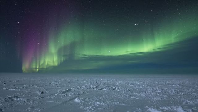 Glowing northern lights sweeping over frozen polar ice field under starry sky
