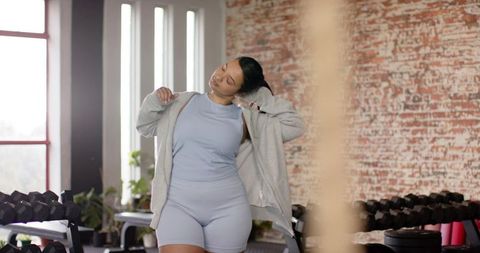 Asian woman stretching and adjusting hoodie in light blue activewear at urban brick gym