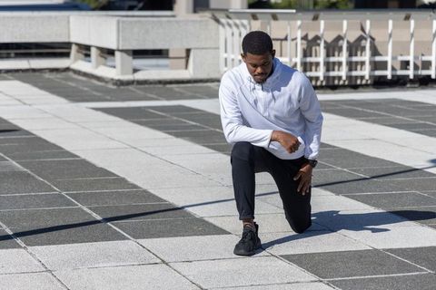 African american male kneeling and stretching on urban rooftop terrace wearing hoodie and sneakers