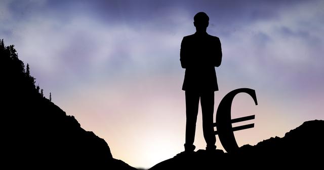Silhouette of businessman with hands on hips standing on mountain summit with a large euro sign, framed by a dramatic dawn sky. Excellent for use in business presentations, financial growth visuals, leadership themes, and motivational materials. Conveys a sense of achievement, economic success, and future prosperity.