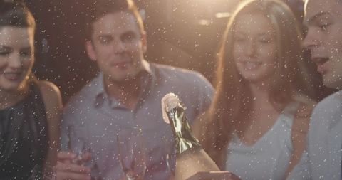 Champagne popping, spraying foam as friends toast with flutes in dim lounge celebration