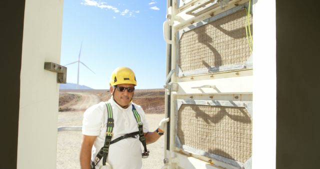 Engineer in safety gear standing next to the entrance of a wind turbine, representing clean energy solutions. Ideal for topics on renewable energy, wind power, engineer professions, safety standards in work environments, and promoting sustainable energy sources.