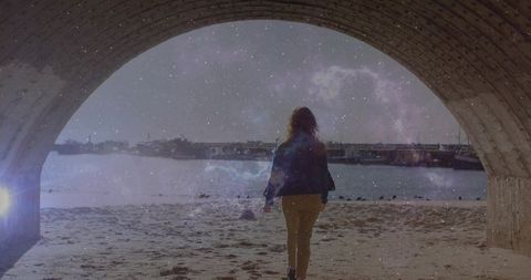 Woman walking through concrete arch toward harbor beach under starry nebula overlay