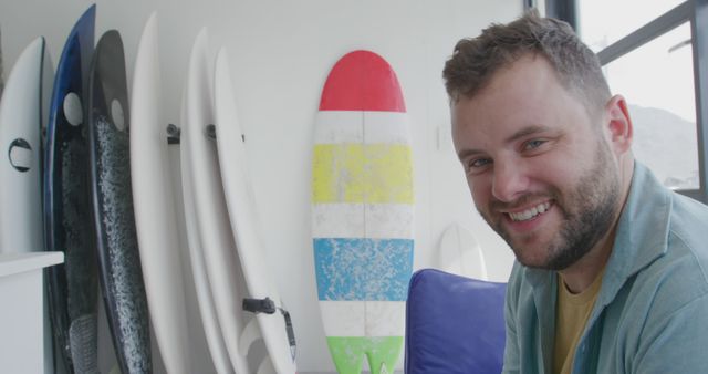 Caucasian man smiles beside a collection of surfboards, with copy space. His cheerful expression suggests a passion for surfing and beach lifestyle at home.