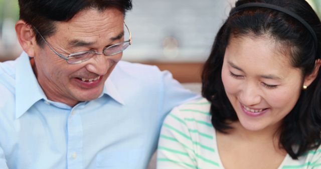 A middle-aged Asian man and woman share a joyful moment together, with copy space. Their smiles and close proximity suggest a strong bond, indicating a family connection or a close friendship.