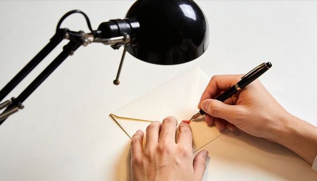 Hands sealing envelope with red wax using fountain pen under desk lamp soft light