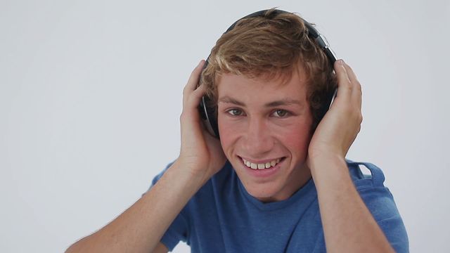 Young man smiling while listening to music with headphones. Ideal for ads or articles about music, lifestyle, youth enjoyment, and modern gadgets. Great for illustrating themes of relaxation, positive moments, and audio experiences.