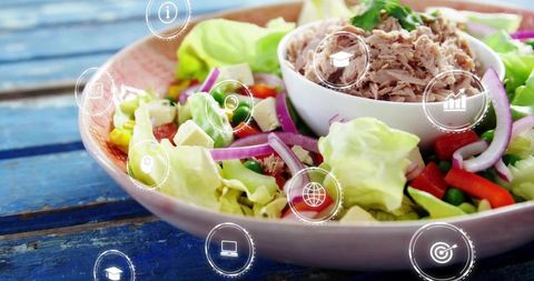 Fresh tuna salad in ceramic bowl on rustic blue wooden table with health icons overlay
