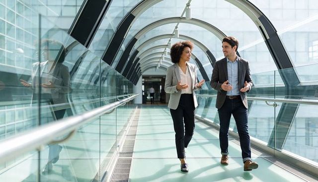 Business duo walking and talking in glass skybridge promoting collaboration modern office