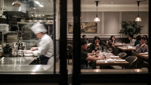 Chef preparing dishes behind glass while diners enjoy intimate modern restaurant ambience