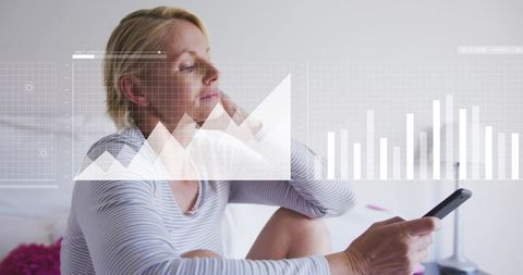 Mature woman viewing floating data charts on smartphone in bedroom after receiving notification