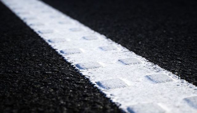 Diagonal white road stripe cutting across black asphalt with raised pavement markers