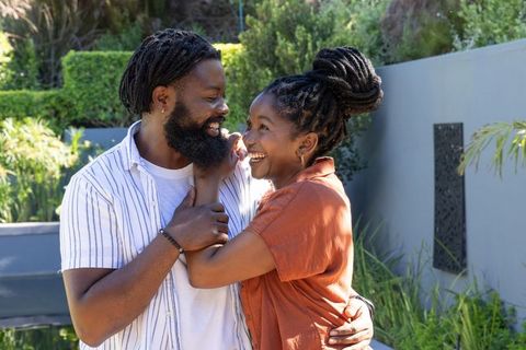 African couple embracing and laughing in sunny landscaped backyard enjoying romantic moment