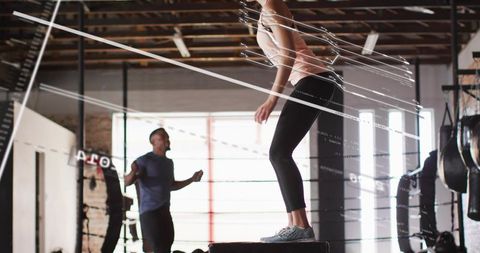 Woman jumping on plyo box with jump rope in industrial gym boxing studio workout