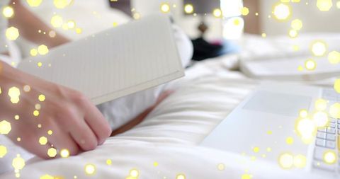 Holding female hand flipping lined notebook on cozy bed with laptop and warm bokeh