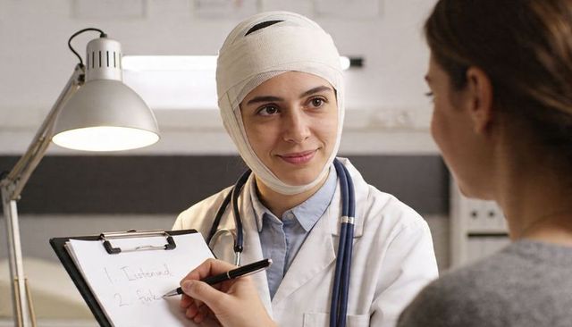 Head-bandaged clinician listening attentively during patient consultation with stethoscope